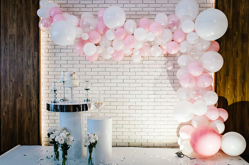 Photo-wall, wedding decoration space or place from white and pink balloons and white brick wall near table with a wedding cake, candles and flowers.