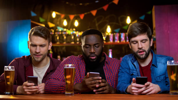 Multiethnic friends using smartphones sitting in pub, problem with communication Multiethnic friends using smartphones sitting in pub, problem with communication friends in bar with phones stock pictures, royalty-free photos & images