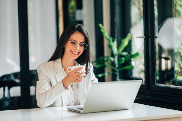 istock Elegant young woman using laptop and drinking coffee in modern office. 1159564108
