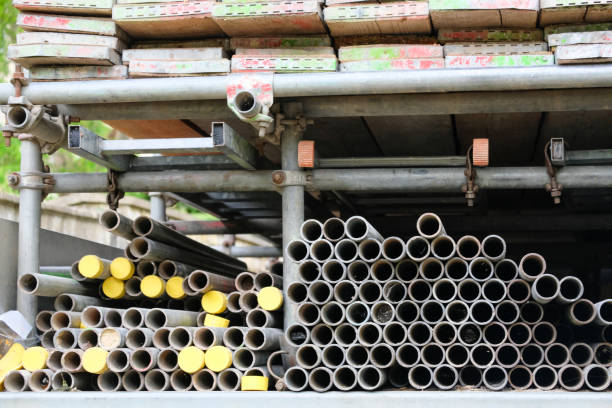 Wooden scaffolding boards and long metal tubes, some with yellow rubber caps on the end, stored on the back of a builders lorry. All stored neatly within a scaffolding frame structure, with different sized lightweight ladders lying flat in the middle section. Scaffolding fittings secure the frame and keep everything in position for transportation.
