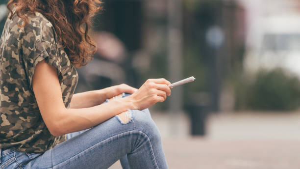 giovane donna che tiene in mano un giunto di marijuana, pronta a fumare. fumo urbano di disomodi. - narcotic teenager marijuana drug abuse foto e immagini stock