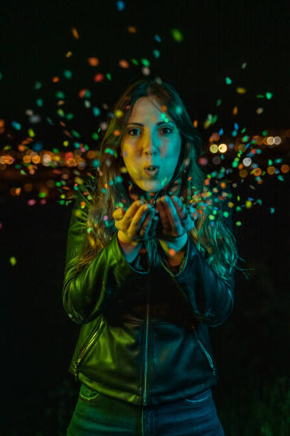 istock Young woman blowing confetti at night party 1159569808