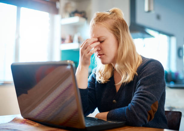 Tired young blonde woman taking a break from using laptop A pretty young blonde using a laptop at home stops to rub her tired eyes, perhaps suffering from a headache. eye-strain stock pictures, royalty-free photos & images