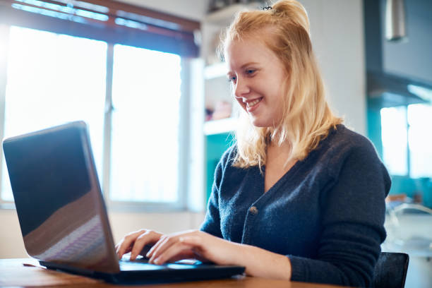 istock Pretty, smiling blonde using laptop at home 1159570395