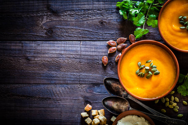 Pumpkin soup with ingredients on rustic wooden table with copy space Two brown bowls filled with homemade pumpkin soup surrounded by ingredients for preparing soup shot from above on rustic wooden brown table. Predominant colors are orange and brown. The composition is at the right of an horizontal frame leaving a useful copy space for text and/or logo. Predominant colors are orange and brown. Low key DSRL studio photo taken with Canon EOS 5D Mk II and Canon EF 100mm f/2.8L Macro IS USM. pumpkin soup photos stock pictures, royalty-free photos & images