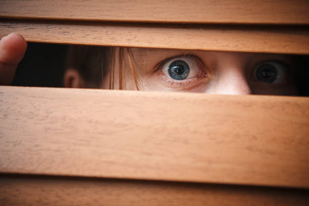 istock Frightened girl peeping through wooden venetian blinds 1159572323