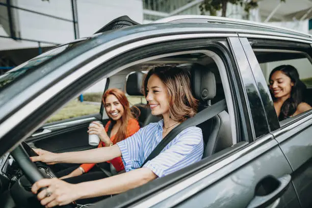 Young women driving in car - sharing a ride to work or going for a road trip together.