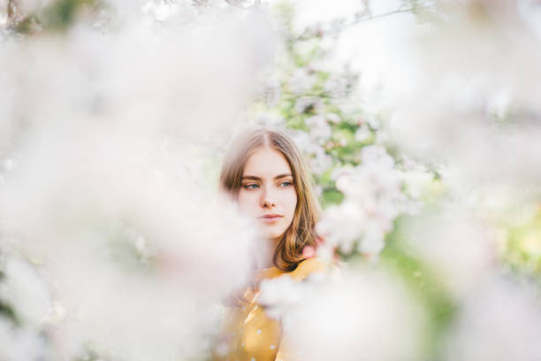 Beautiful young blonde posing in the countryside next to a blossoming tree in spring.