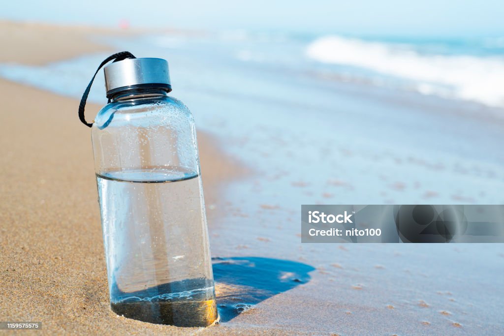 reusable water bottle on the beach closeup of a glass reusable water bottle on the seashore of a lonely beach Water Bottle Stock Photo