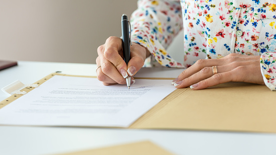 Closeup of businesswoman with perfect french manicure signing a contract or document in a folder.