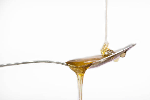 istock Honey dripping from a silver spoon on isolated white background 1159581602