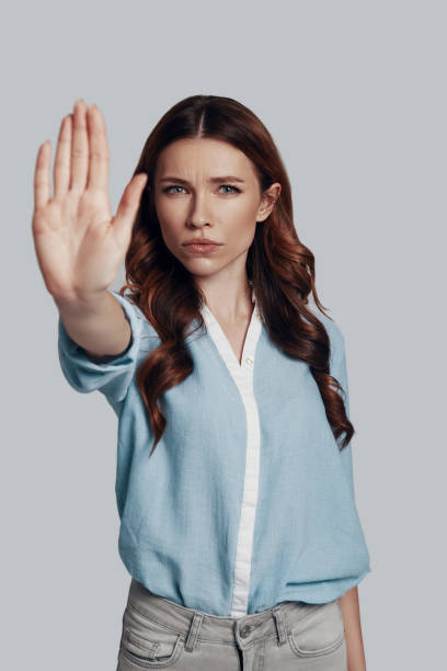 istock Stop! Attractive young woman looking at camera and gesturing while standing against grey background 1159585249