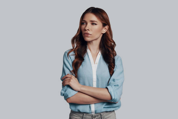 istock Lost in thoughts. Beautiful young woman looking away while standing against grey background 1159585512