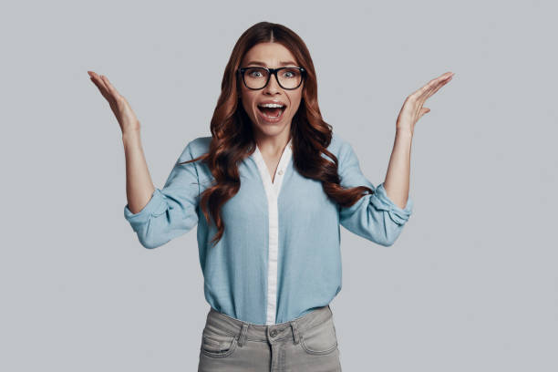 istock Surprise! Attractive young woman looking at camera and gesturing while standing against grey background 1159586704