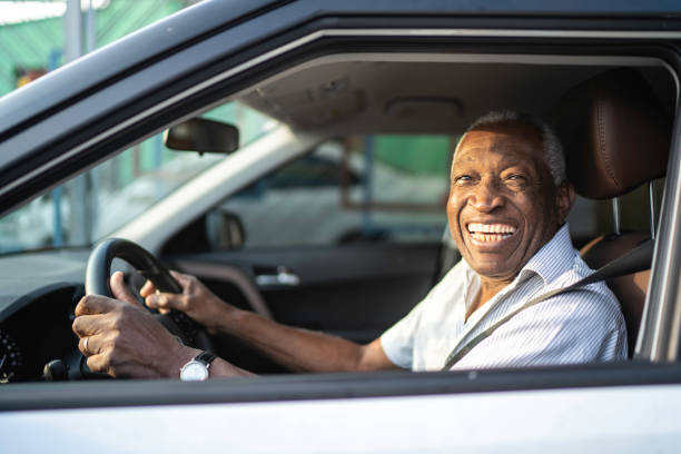 sorridente uomo afro anziano alla guida di un'auto e guardando la telecamera - side window foto e immagini stock