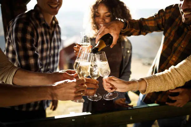 Close up of happy friends having fun while drinking champagne on a terrace party. One of them is pouring.