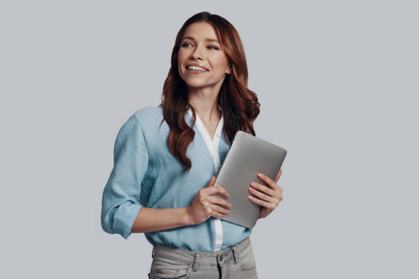 istock Doing business. Attractive young woman looking away and smiling while standing against grey background 1159587389