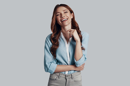 Sincere smile. Attractive young woman looking at camera and smiling while standing against grey background