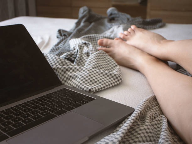 istock Laptop on the bed and female legs. Work at home or dependence on devices 1159592721