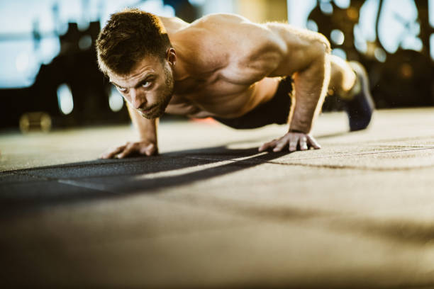 muscular build male athlete exercising push-ups in a gym. - exercising men push ups muscular build imagens e fotografias de stock