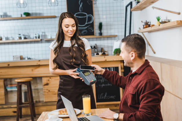 istock attractive waitress holding terminal wile handsome freelancer sitting at table with laptop and paying with smartphone in coffee house 1159599545