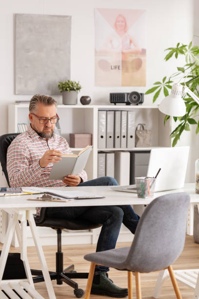 istock Casual looking handsome senior psychologist reading book at his office 1159599621