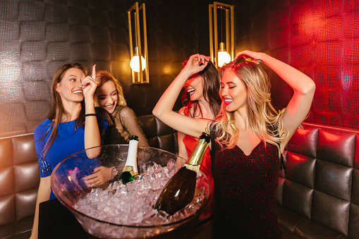 Happy women clinking champagne glasses and celebrating at night club