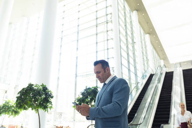 istock Mature Caucasian businessman looking at mobile phone while standing in modern office 1159605749