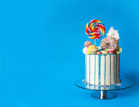 Colorful candy drip cake, blue background, right sided, with copy space. Perfectly usable for all party and fun projects.