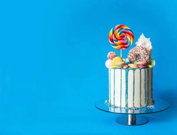 Photo of Colorful candy drip cake, blue background, right sided, with copy space