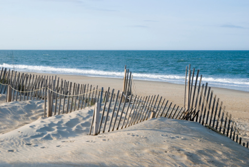Beach fence and sand dunes with Atlantic Ocean horizon, scenic landscape in the Outer Banks at Nags Head, North Carolina, USA.