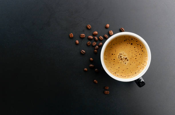 espresso caliente y grano de café en la mesa negra con enfoque suave y sobre la luz en el fondo. vista superior - café edificio de hostelería fotografías e imágenes de stock