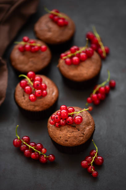 Chocolate muffins decorated red currant berries on dark wooden background. Flat lay. Soft focus
