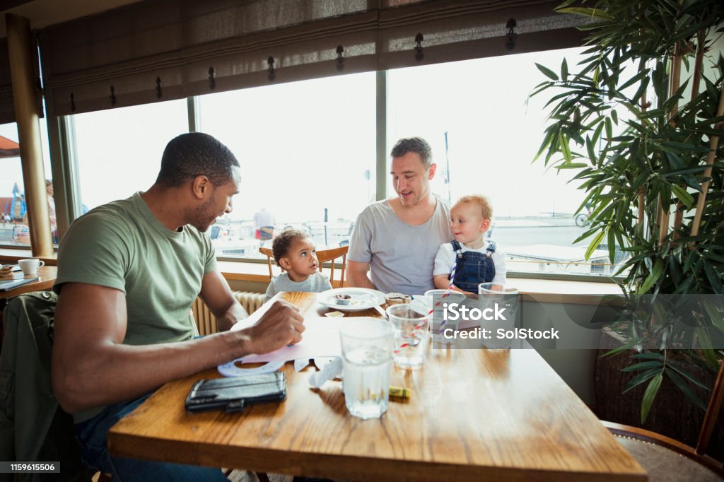 Friends and Sons Having Lunch Two men with their sons sitting at a table enjoying lunch together. Cafe Stock Photo