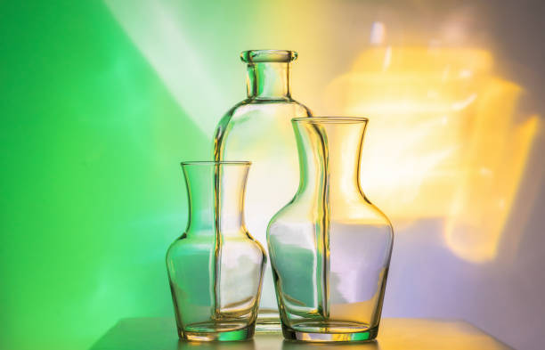 istock Glass transparent tableware - bottles of different sizes, three pieces on a beautiful multi-colored, yellow, and green, background. very beautiful still life. 1159616710