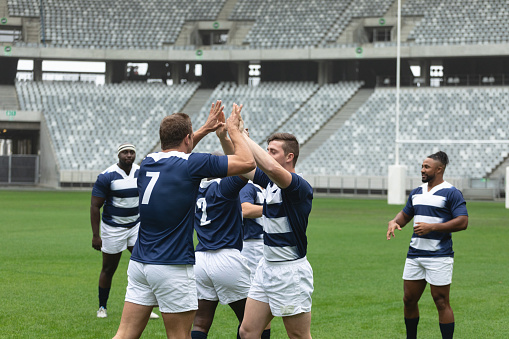 Side view of group of diverse male rugby players celebrating goal in stadium