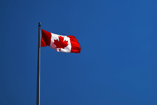 Canadian flag flying in light breeze on top of metal pole against blue sky, close-up