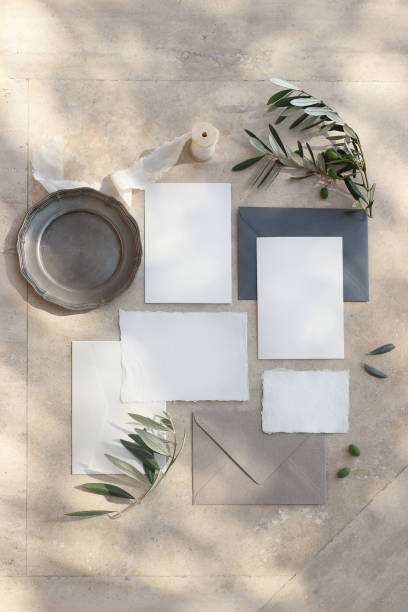 istock Summer wedding stationery mock-up scene. Blank greeting cards, envelopes, silver plate, silk ribbon and olive branches in sunlight. Marble background with shadows. Vertical feminine flat lay, top view 1159624430