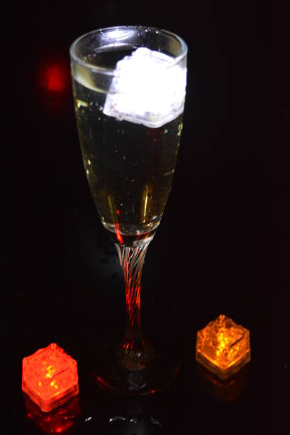 wielokolorowe świecące kostki lodu unoszą się w kryształowym kieliszku do szampana, który oświetla napój w nim. - wineglass glass crystal studio shot zdjęcia i obrazy z banku zdjęć