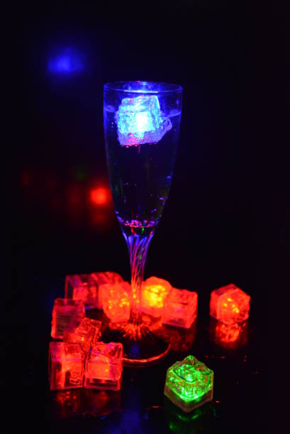 istock Multicolored glowing ice cubes float in a crystal champagne glass that illuminates the drink in it. 1159626121