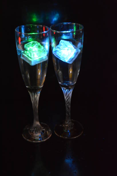 Multicolored glowing ice cubes float in a crystal champagne glass that illuminates the drink in it.