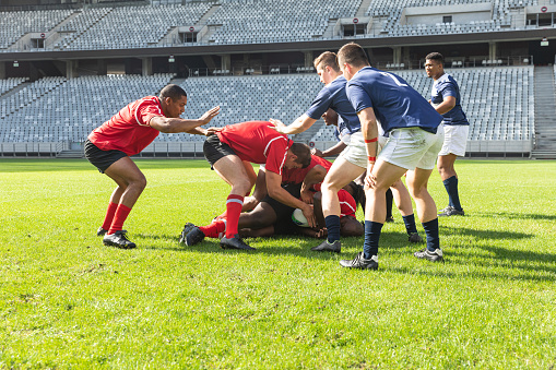 Front view of group of diverse male rugby players playing rugby match in stadium. Players are trying to get the ball from each other.