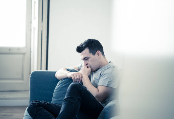 Portrait of young man felling depressed and desperate crying alone in sofa home suffering emotional pain and unhappiness. In People Broken heart, Bullying Depression and Mental health issues concept. stock photo