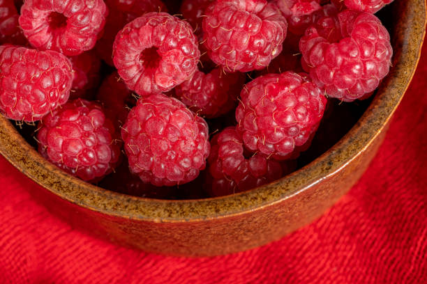 A clay bowl filled with red raspberries