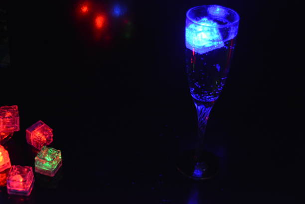 istock Multicolored glowing ice cubes float in a crystal champagne glass that illuminates the drink in it. 1159629162