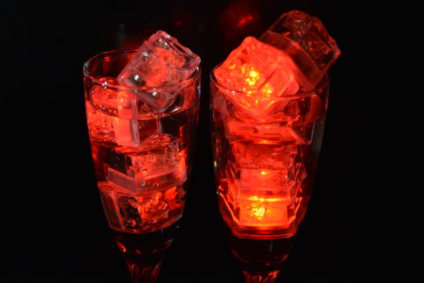 Photo of Two unusual glasses of champagne with a drink and bright red ice chips. Plastic ice cubes of ice illuminating the drink in each glass on a black background, an impressive photo and the feast of St. Valentine, the holiday of all lovers.