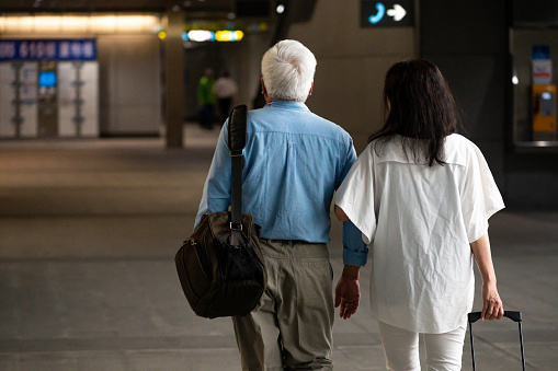 Rear view of senior business couple walking at subway station. Male and female colleagues are with luggage. They are on business trip.