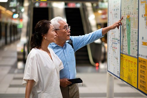 Businesswoman looking at businessman pointing on map. Senior business couple are standing at subway station. They are on business trip.