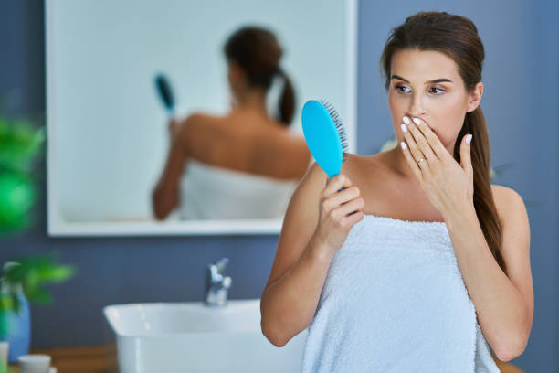 Happy woman brushing hair in bathroom having problem with hair loss Adult woman brushing her hair in bathroom fen photos stock pictures, royalty-free photos & images