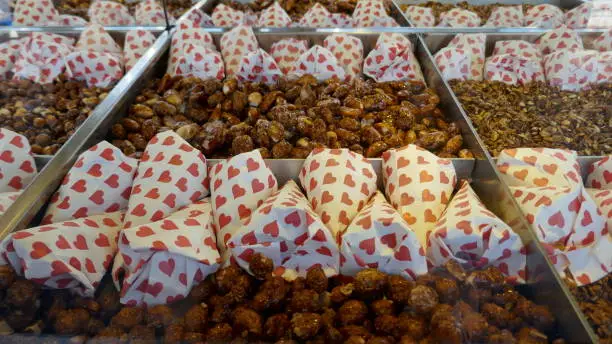 Roasted and caramelized almonds, loose and in white paper bags with red heart pattern on the market for sale.